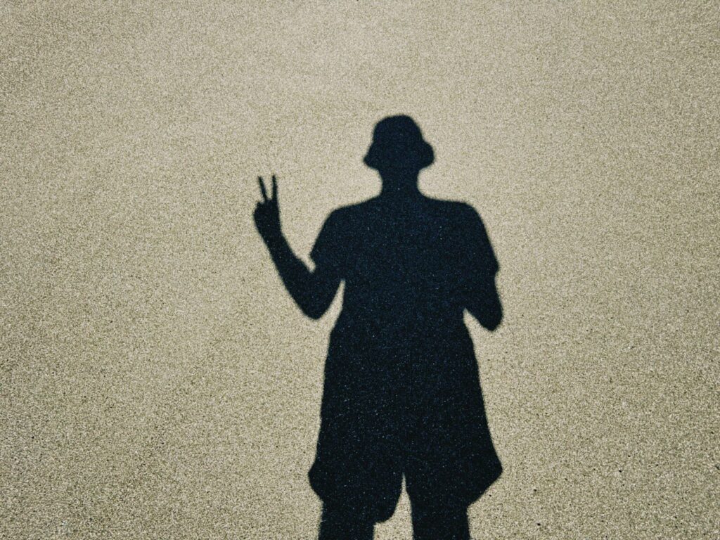 Shadow of a person wearing a hat making peace sign