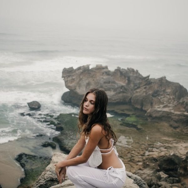 Woman in white clothes crouching on rocks by the ocean